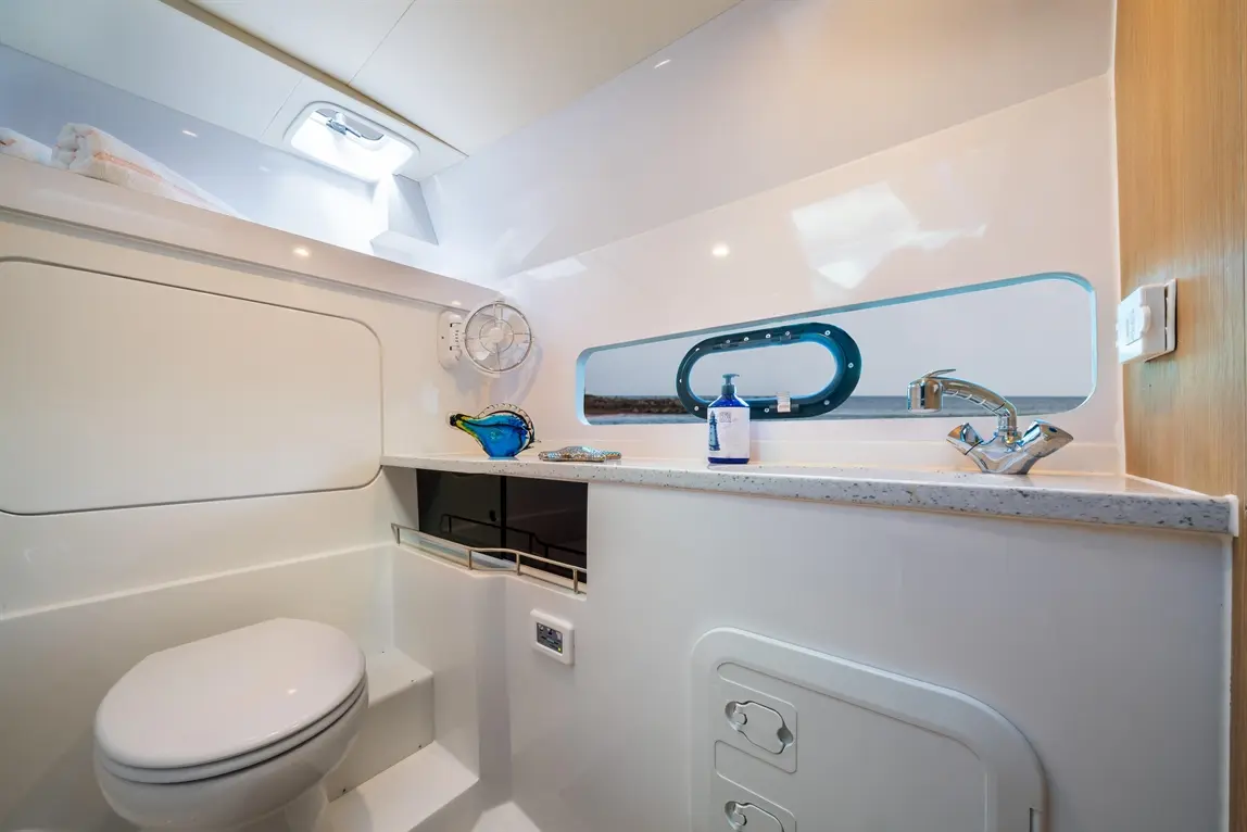 Modern bathroom interior featuring a toilet, sink, decorative glass items, and a window with natural light.
